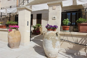 Une cour avec de grands pots en céramique remplis de fleurs, un mur en pierre et une rambarde en métal.