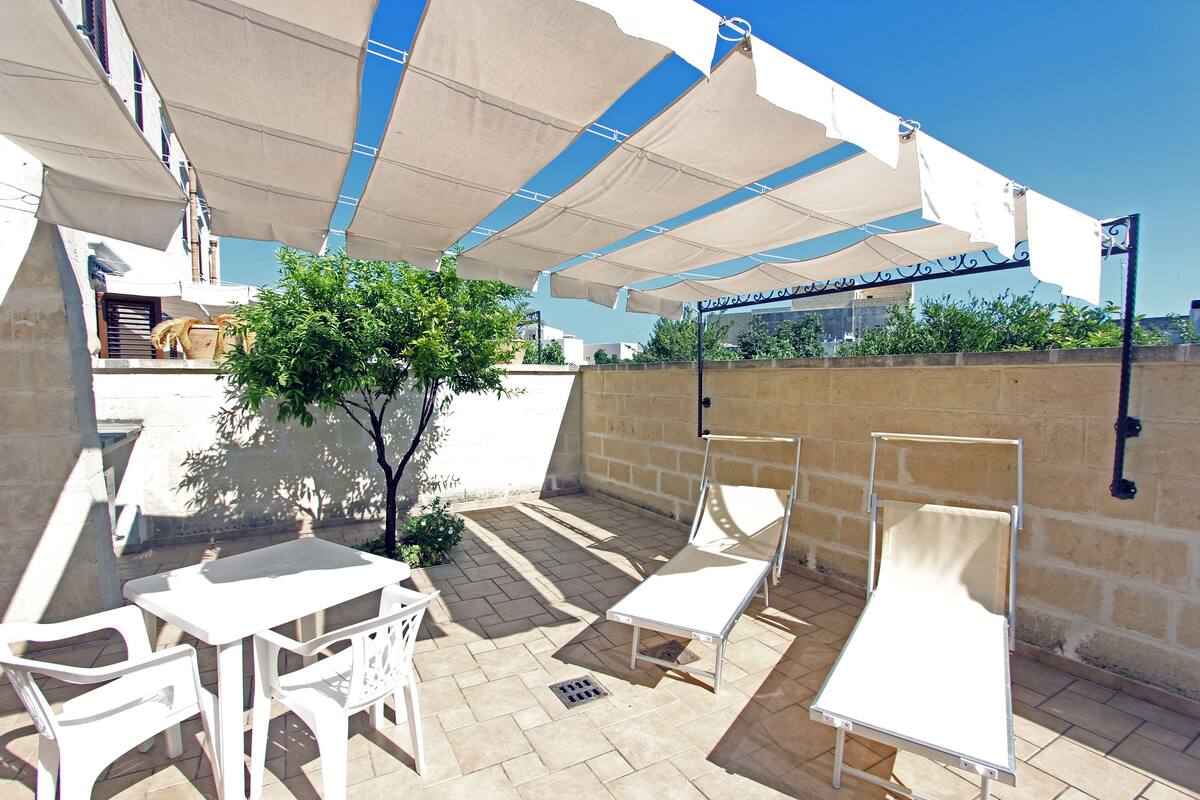 An outdoor patio with white furniture, a tree, and a wall with a metal railing.