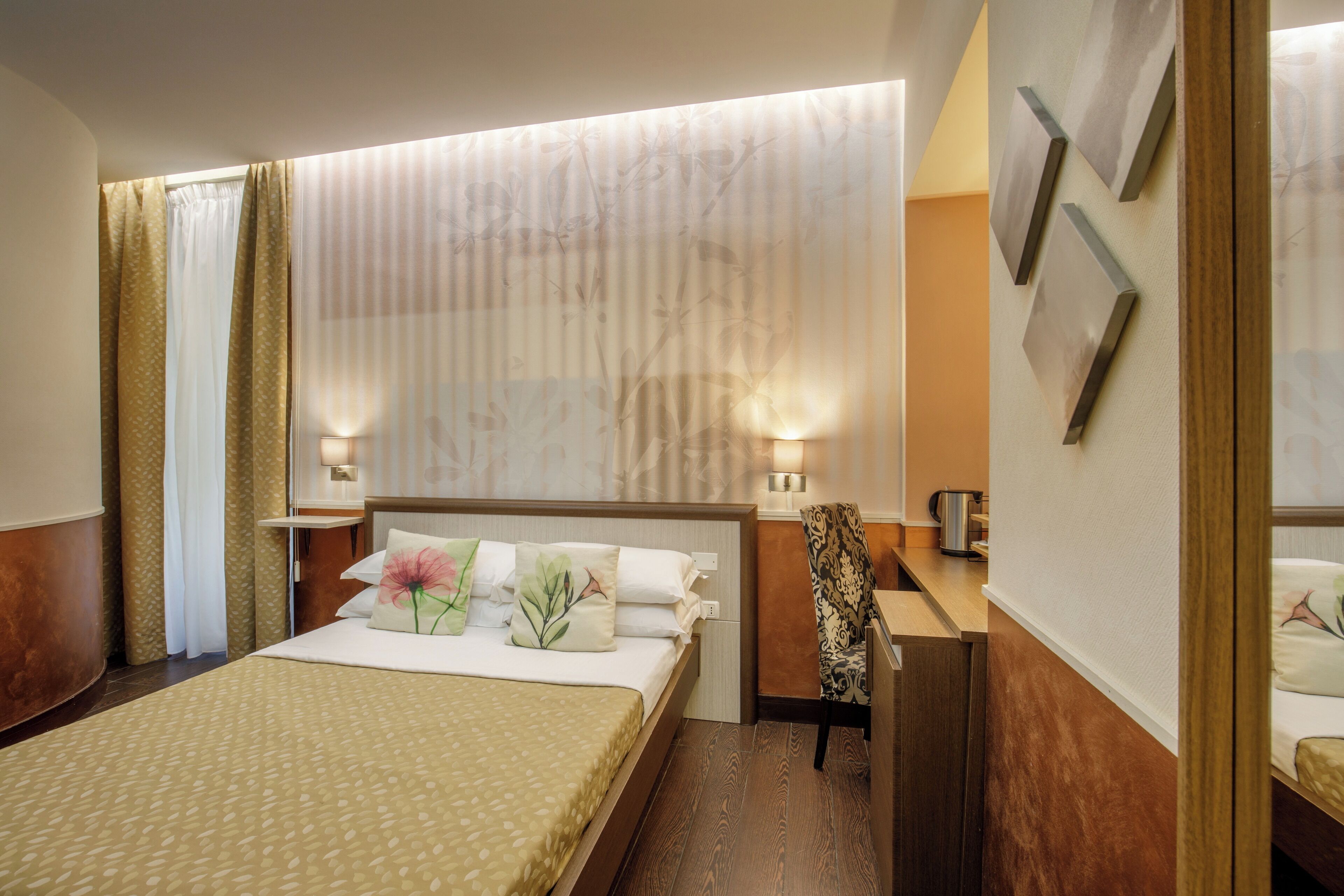 A hotel room with a bed, bedside tables, a chair, and a wall-mounted TV.