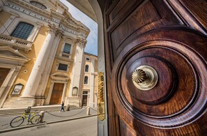 A historic building facade with classical architecture, a large wooden door with a decorative knob, and a bicycle parked in front. - Corso Grand Suite (Rome)