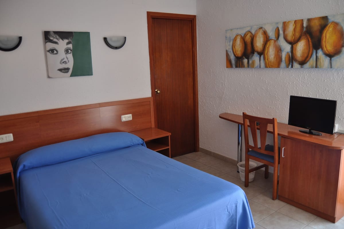 Una habitación de hotel con cama, escritorio con silla, televisión y obras de arte en las paredes.