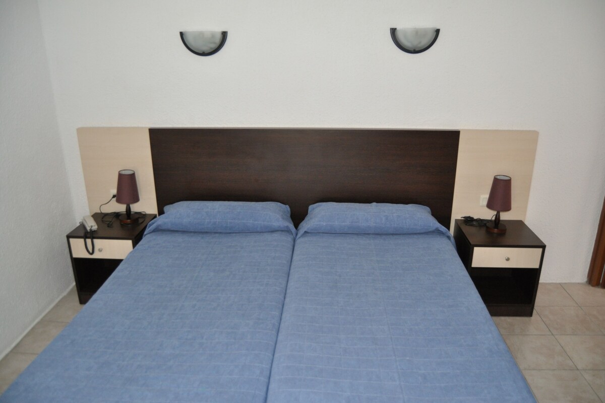 A double bed with a dark headboard, two bedside tables with lamps, and wall sconces.