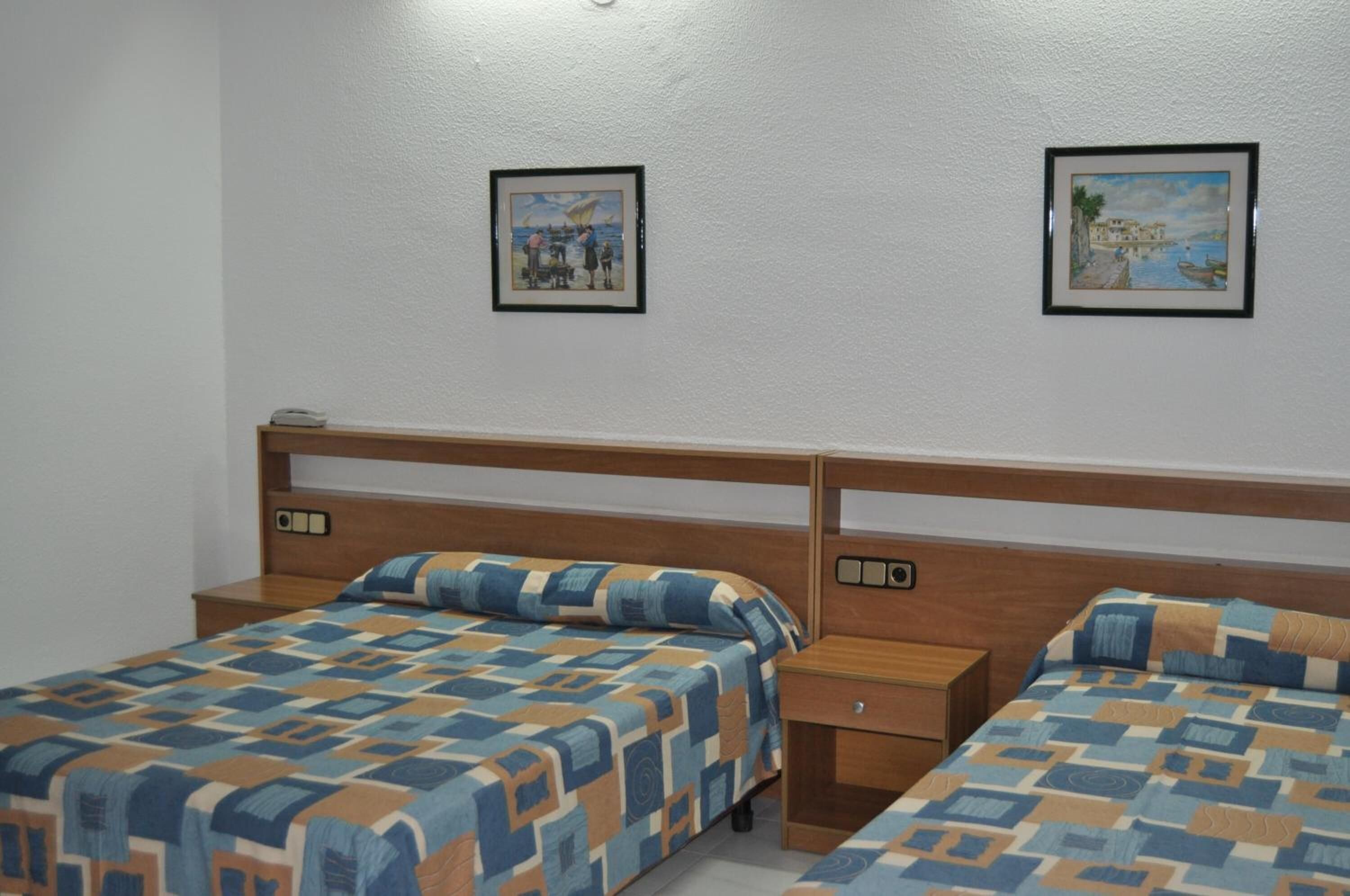 A hotel room with two beds, wooden headboards, and two framed pictures on the wall.