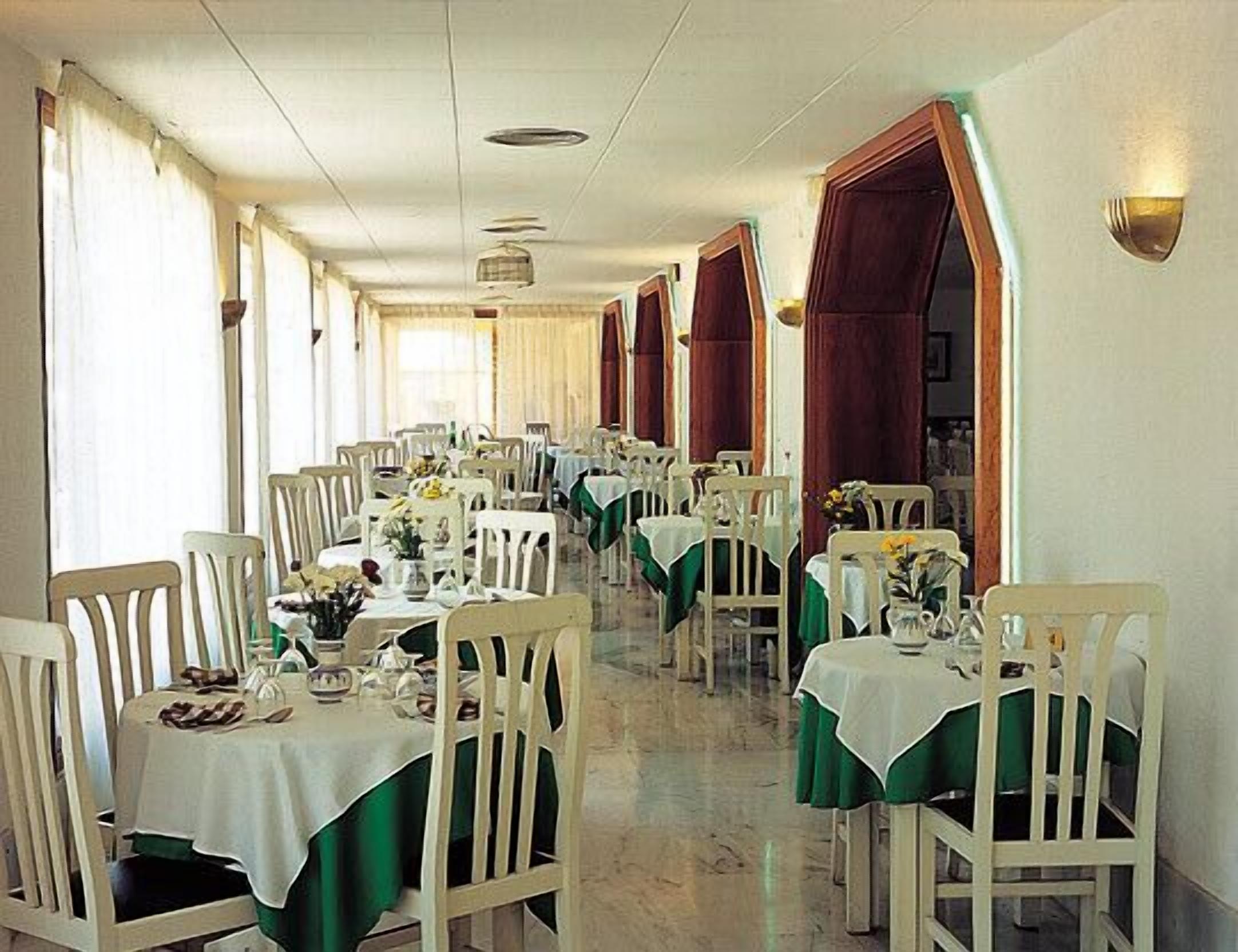 A long dining hall with rows of tables and chairs, each set with a tablecloth and a vase of flowers.