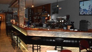 A bar area with a marble countertop, multiple stools, and a variety of bottles and glasses. - Hotel Nautilus (Roses)
