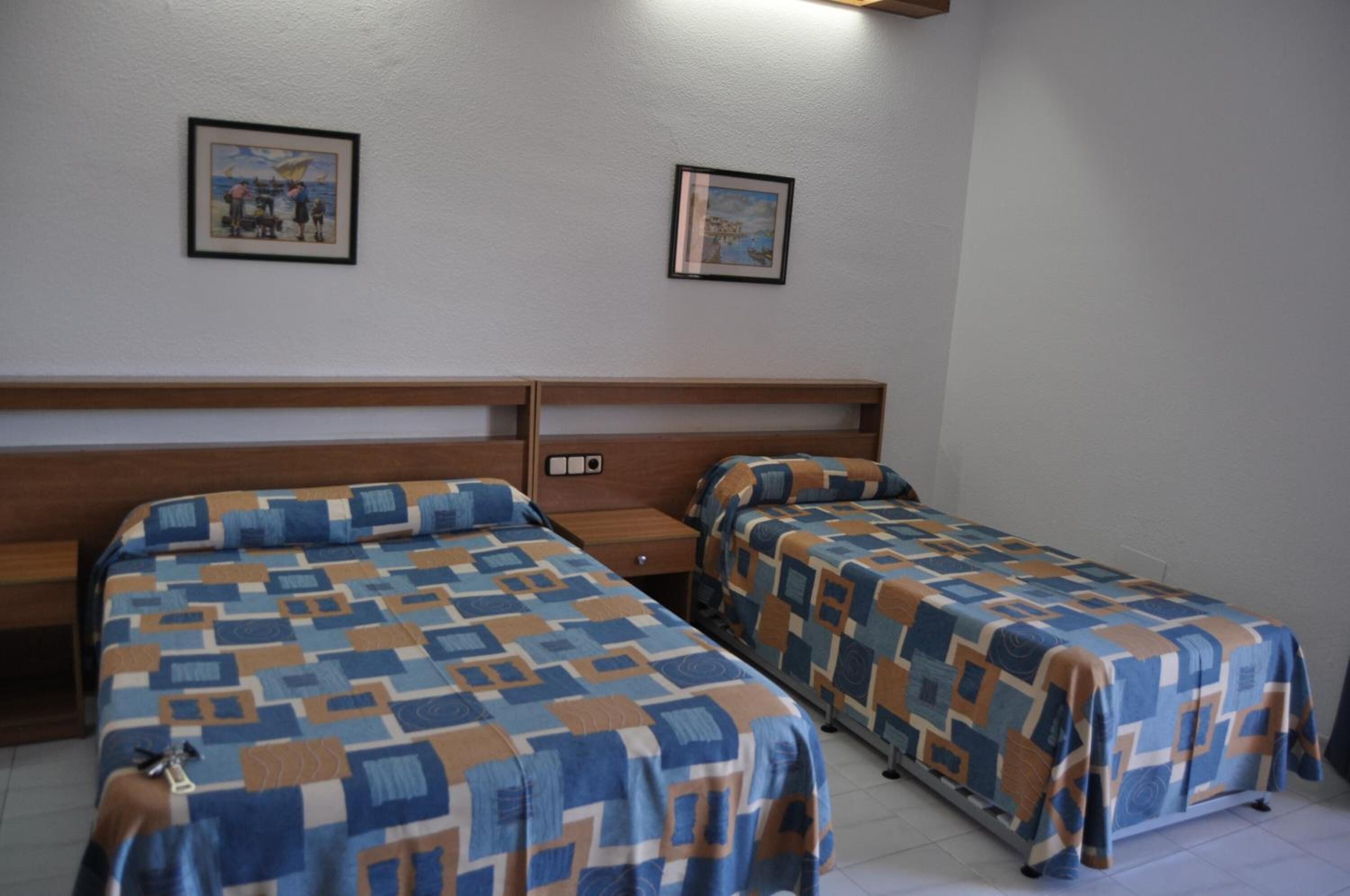 Une chambre avec deux lits simples, des têtes de lit en bois et deux tableaux encadrés au mur.