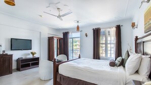 A bedroom with a large bed, a television, a desk, and a window with curtains. - Safira River Front Resort (Morjim)