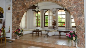 A room with stone walls, a bench, a table, and a window with curtains. - Alkion Hotel (Chania)