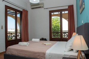 A hotel room with a bed, a lamp, and a view of greenery through the windows. - Alkion Hotel (Chania)