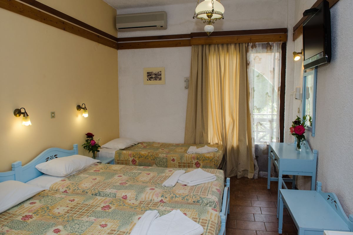 A hotel room with two beds, a desk, a chair, a TV, and a window with curtains.