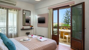 A hotel room with a bed, a TV, a balcony with a table and chairs, and a view of the outdoors. - Alkion Hotel (Chania)