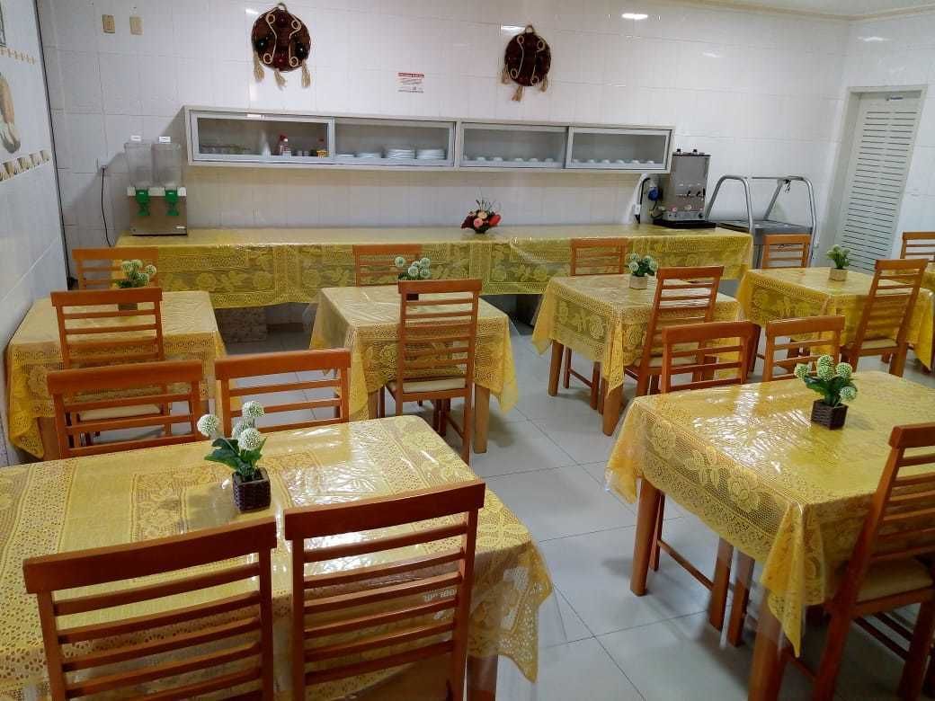 A dining area with multiple tables covered with yellow tablecloths, wooden chairs, and a counter with a water dispenser.
