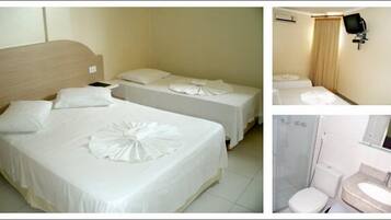 Habitación de hotel con dos camas, un baño con lavamanos e inodoro, y un televisor fijado a la pared.