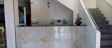 A reception area with a marble counter, a cross on the wall, and a staircase with a metal handrail.