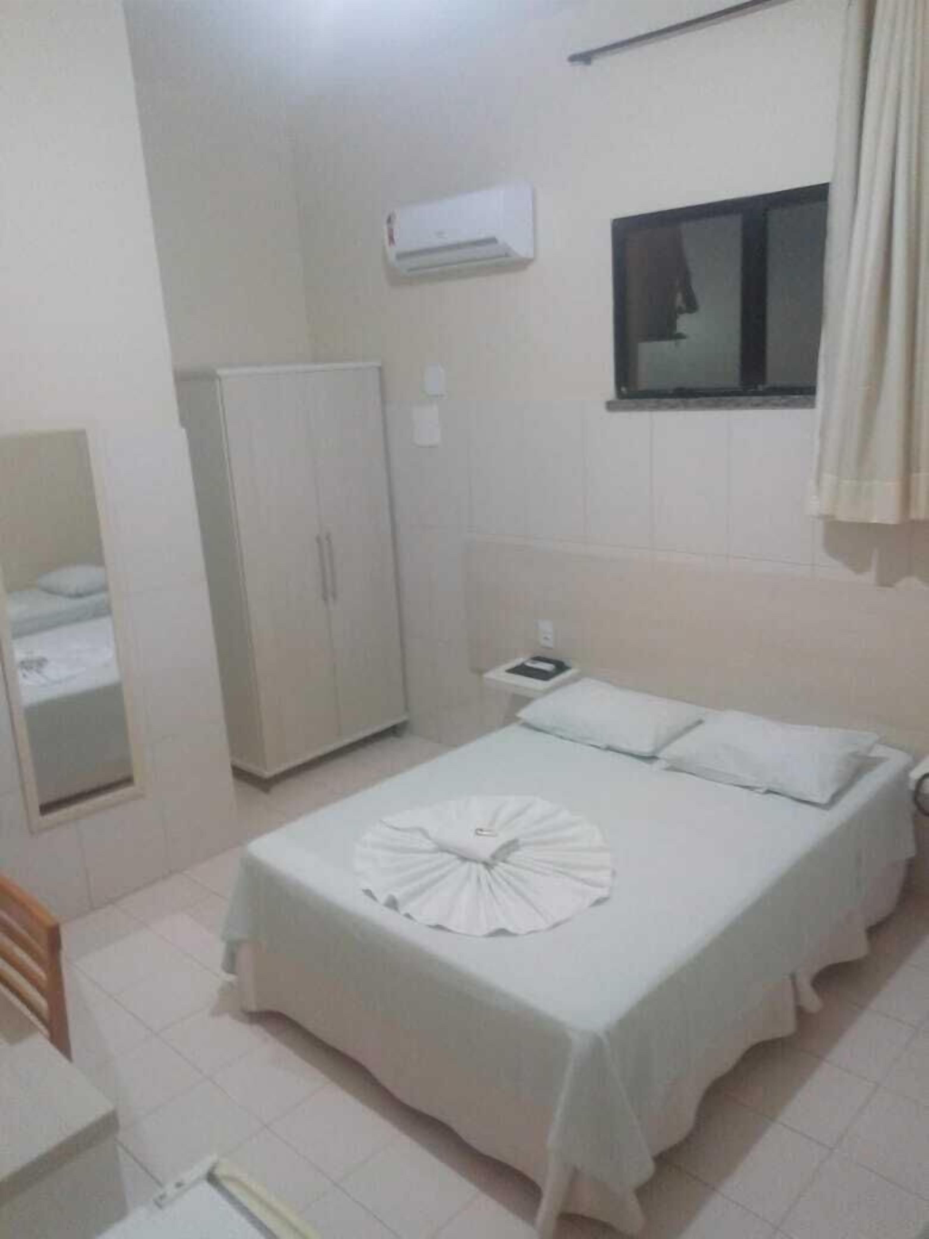 A bedroom with a bed, a wardrobe, a bedside table, a mirror, and an air conditioning unit.