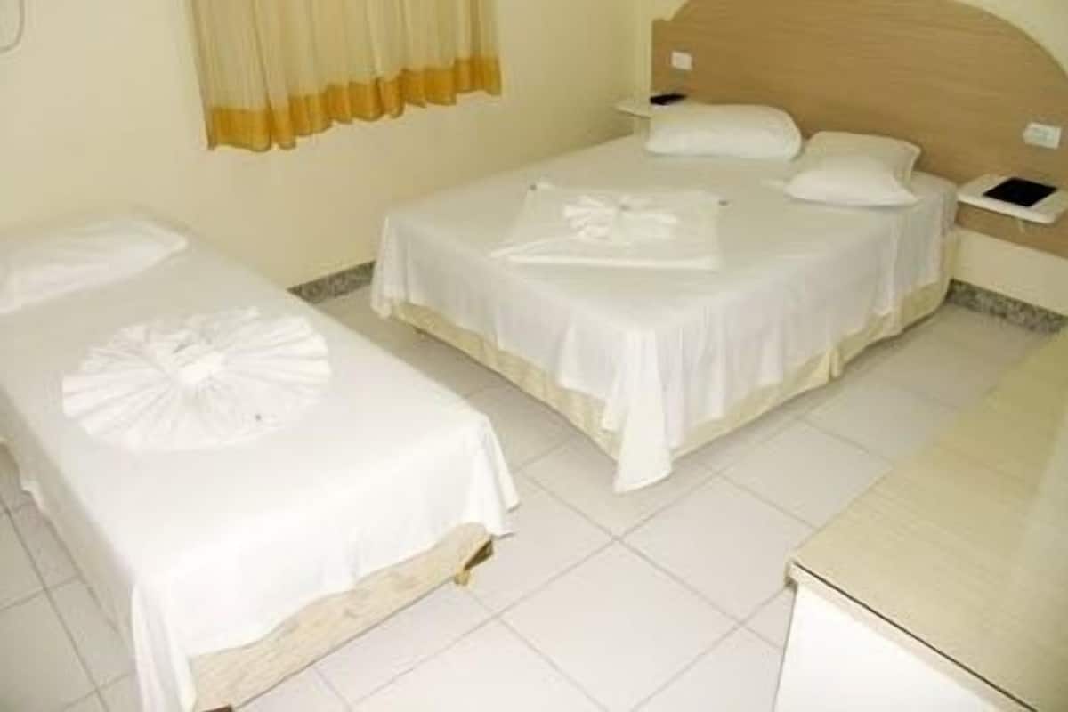 A hotel room with two single beds, a wooden headboard, a bedside table with a lamp, and a small bedside table with a phone.