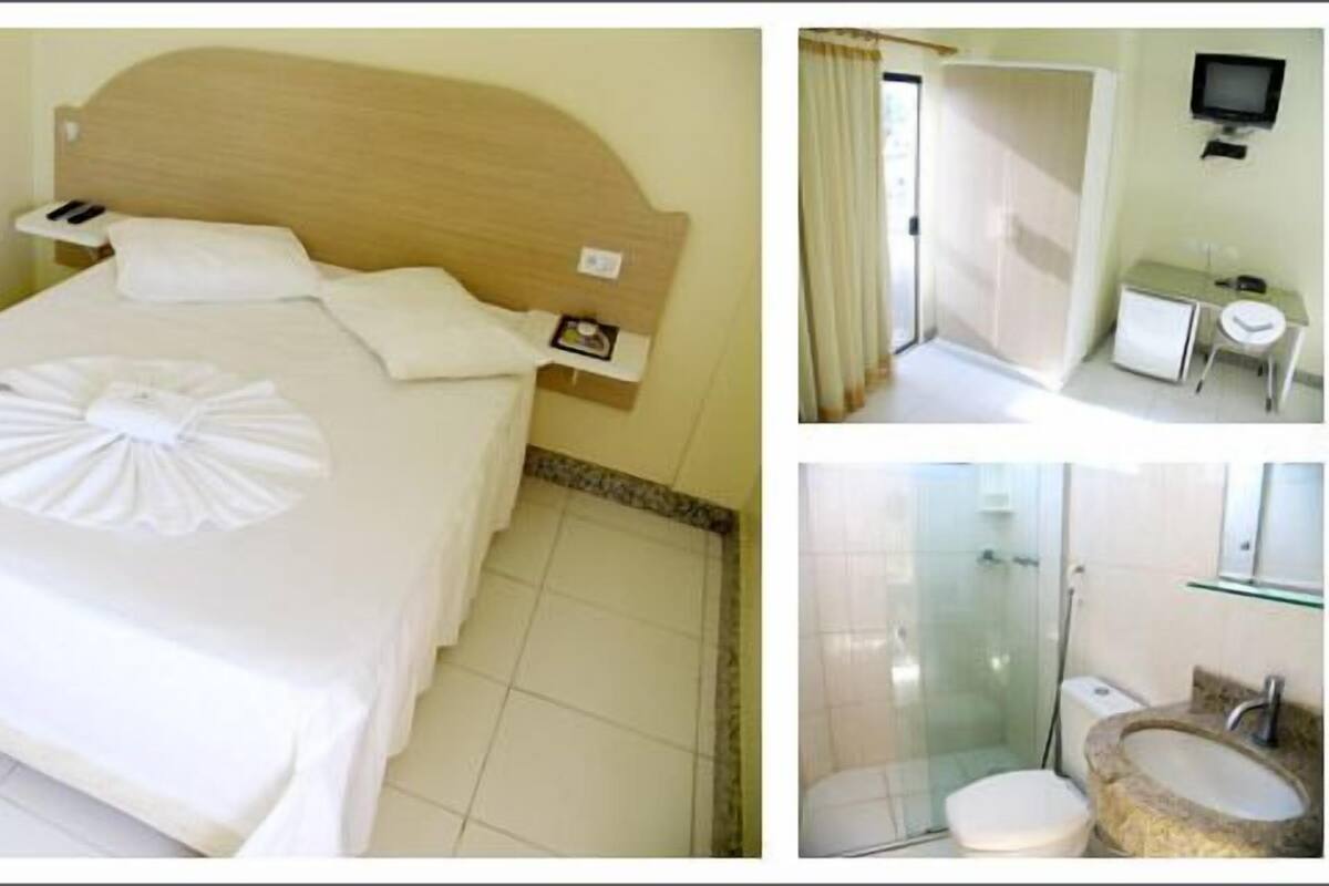 A hotel room with a neatly made bed, a small desk with a chair, a television, and a bathroom with a glass shower and sink.