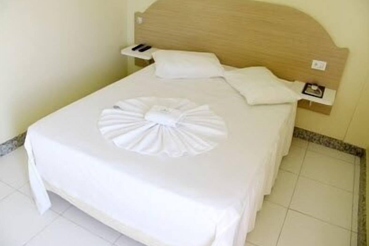 A neatly made bed with a wooden headboard, a white pillow, and a decorative white towel on the bed.