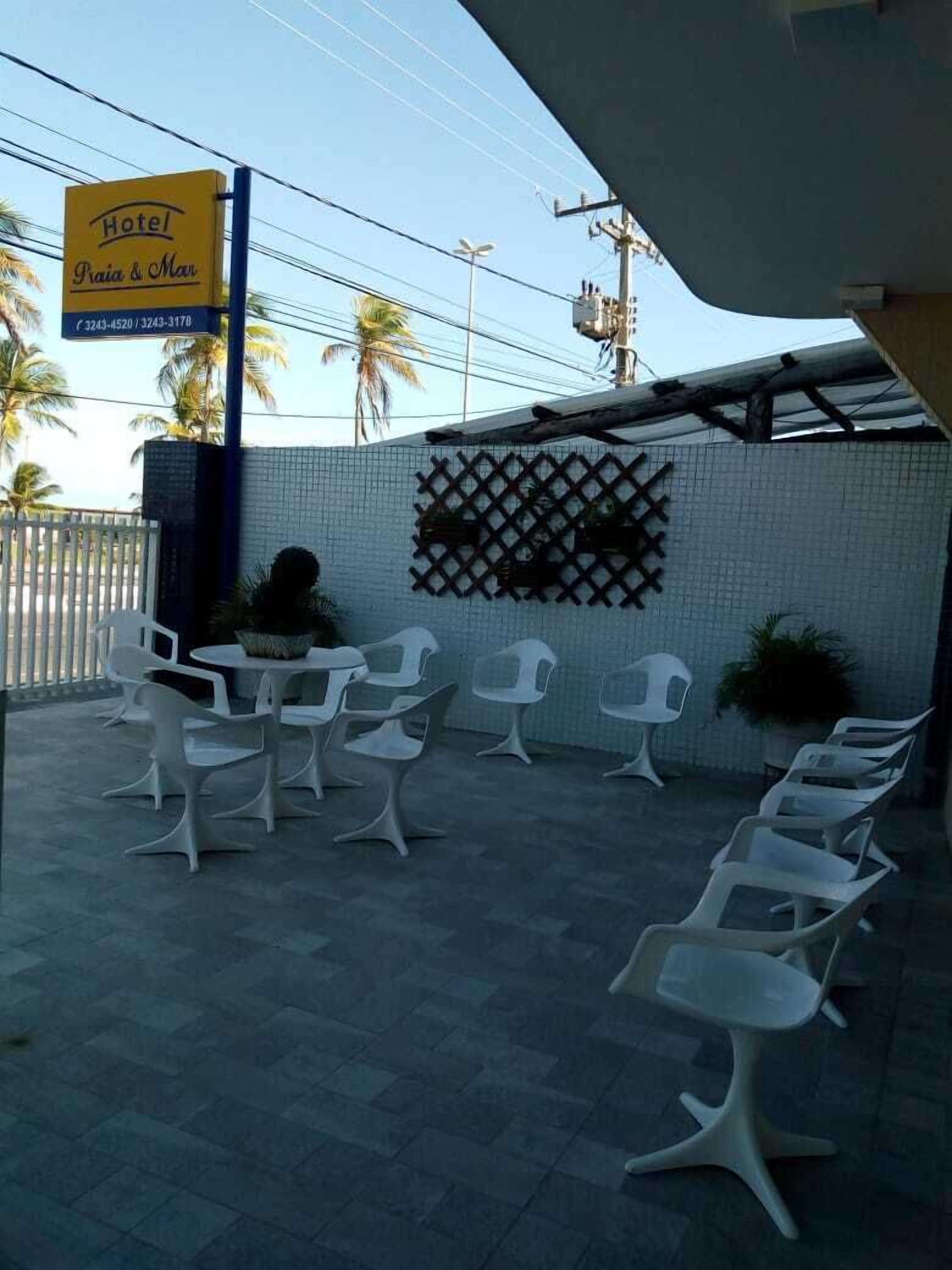 A hotel patio with white plastic chairs arranged around a central table, a decorative lattice wall, and a sign indicating the hotel's name.