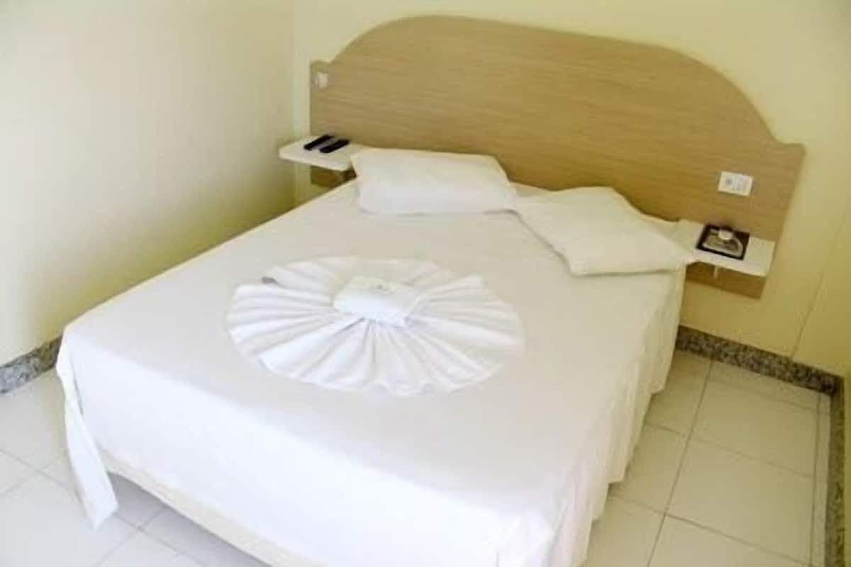 A neatly made bed with a white bedspread and a decorative white towel on the bed.