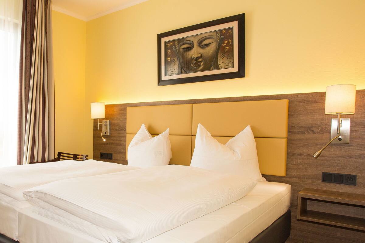 Quarto de hotel com uma cama grande, duas luminárias de cabeceira, uma obra de arte emoldurada acima da cama e cabeceira de madeira.