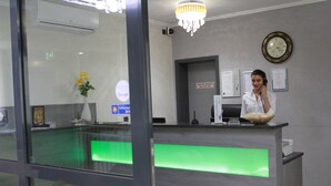 A reception desk with a glass partition, a chandelier, a clock, and a framed certificate on the wall. - Naam Hotel & Apartment Frankfurt City-messe Airpor (Frankfurt)