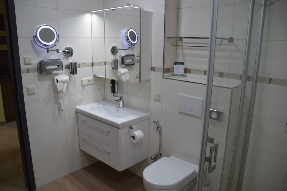 Uma casa de banho moderna com lavatório, espelho, sanita e chuveiro.