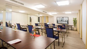 A conference room with multiple tables, chairs, and a large screen. - Naam Hotel & Apartment Frankfurt City-messe Airpor (Frankfurt)