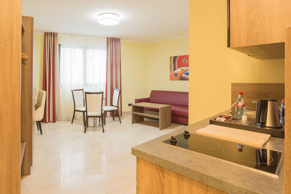 Cozinha moderna com fogão embutido, área de refeições com mesa e cadeiras, e sala de estar com sofá.