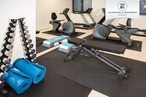 Et fitnesscenter med træningsudstyr, herunder håndvægte, bænk og konditionsmaskiner.