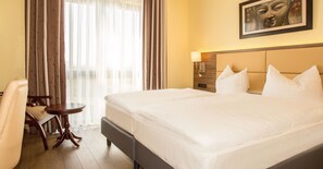 A hotel room with a large bed, a bedside table, a chair, and a window with curtains. - Naam Hotel & Apartment Frankfurt City-messe Airpor (Frankfurt)