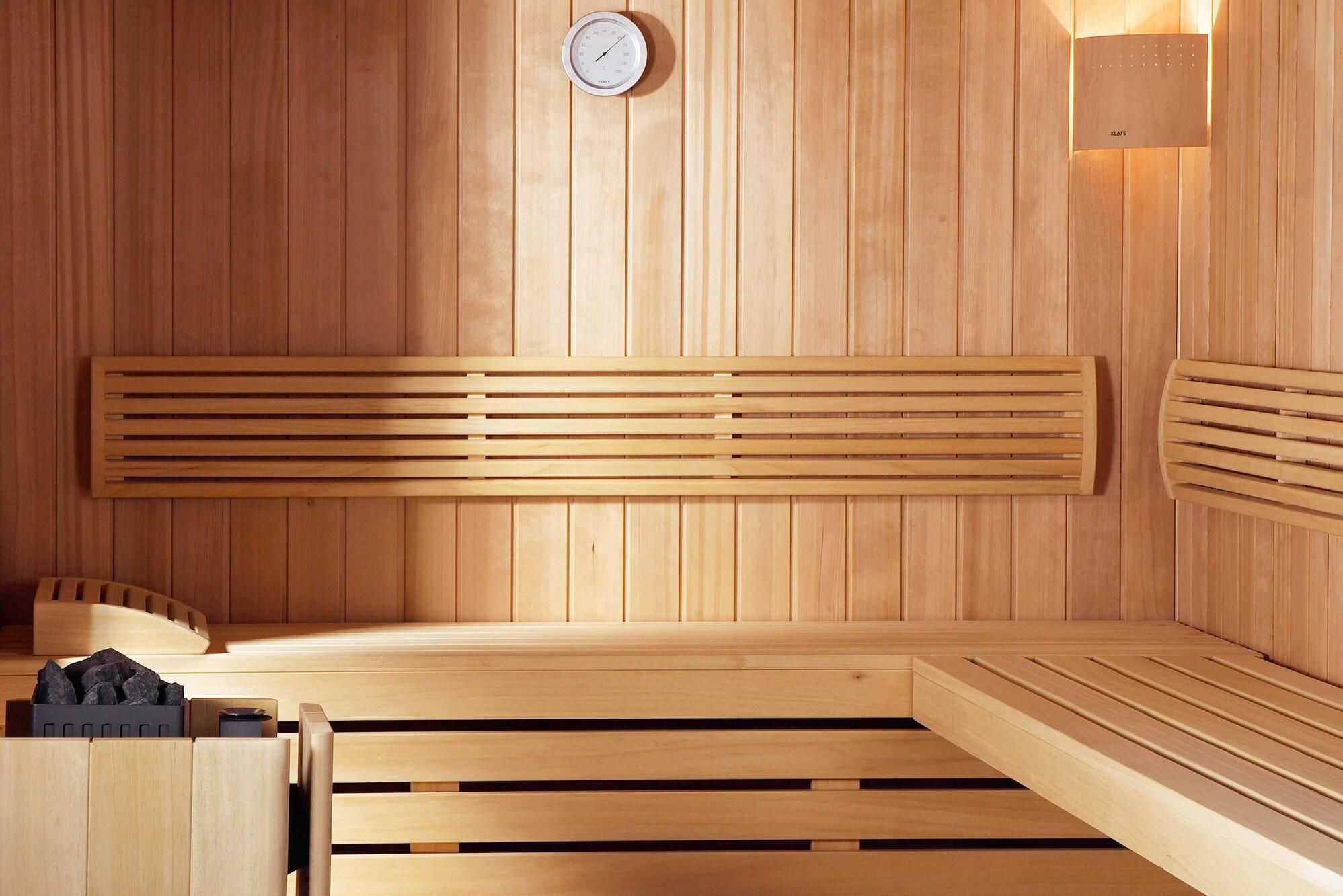 A wooden sauna with benches and a wall-mounted thermometer.
