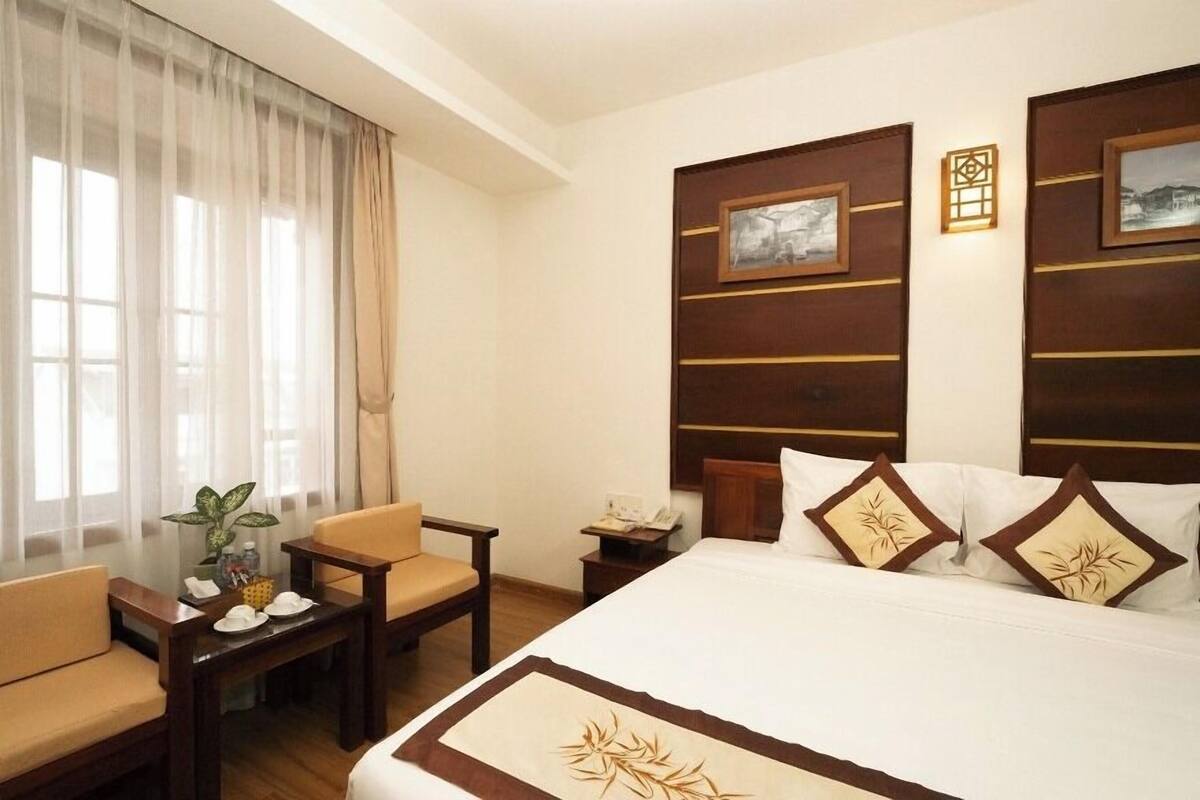 Ein Hotelzimmer mit Bett, zwei Stühlen, einem kleinen Tisch mit Blumenvase und Pflanze sowie einem Nachttisch mit Telefon.
