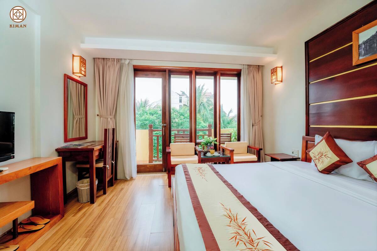 Ein Hotelzimmer mit einem großen Bett, einem Schreibtisch, einem Fernseher, einem Balkon mit Stühlen und Blick ins Grüne.