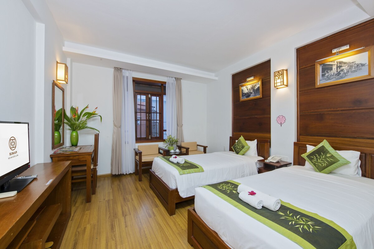A hotel room with two beds, a desk, a TV, and a window with curtains.