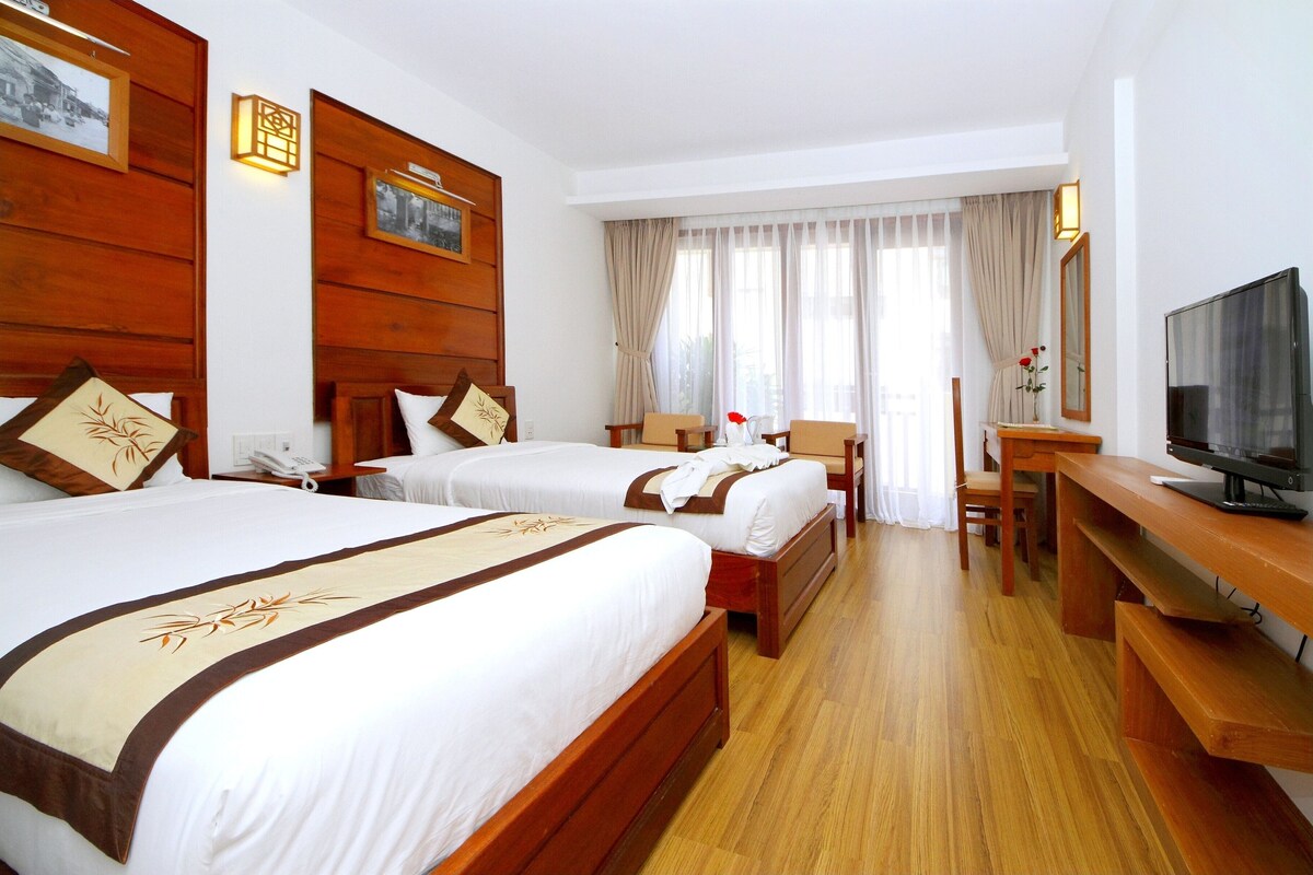 A hotel room with two beds, a desk, a TV, and a window with curtains.