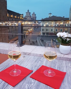 Two glasses of white wine on a table with red napkins, overlooking a cityscape with historic buildings and a view of a square. - Hotel Torre della Vittoria 1928 (Ferrara)
