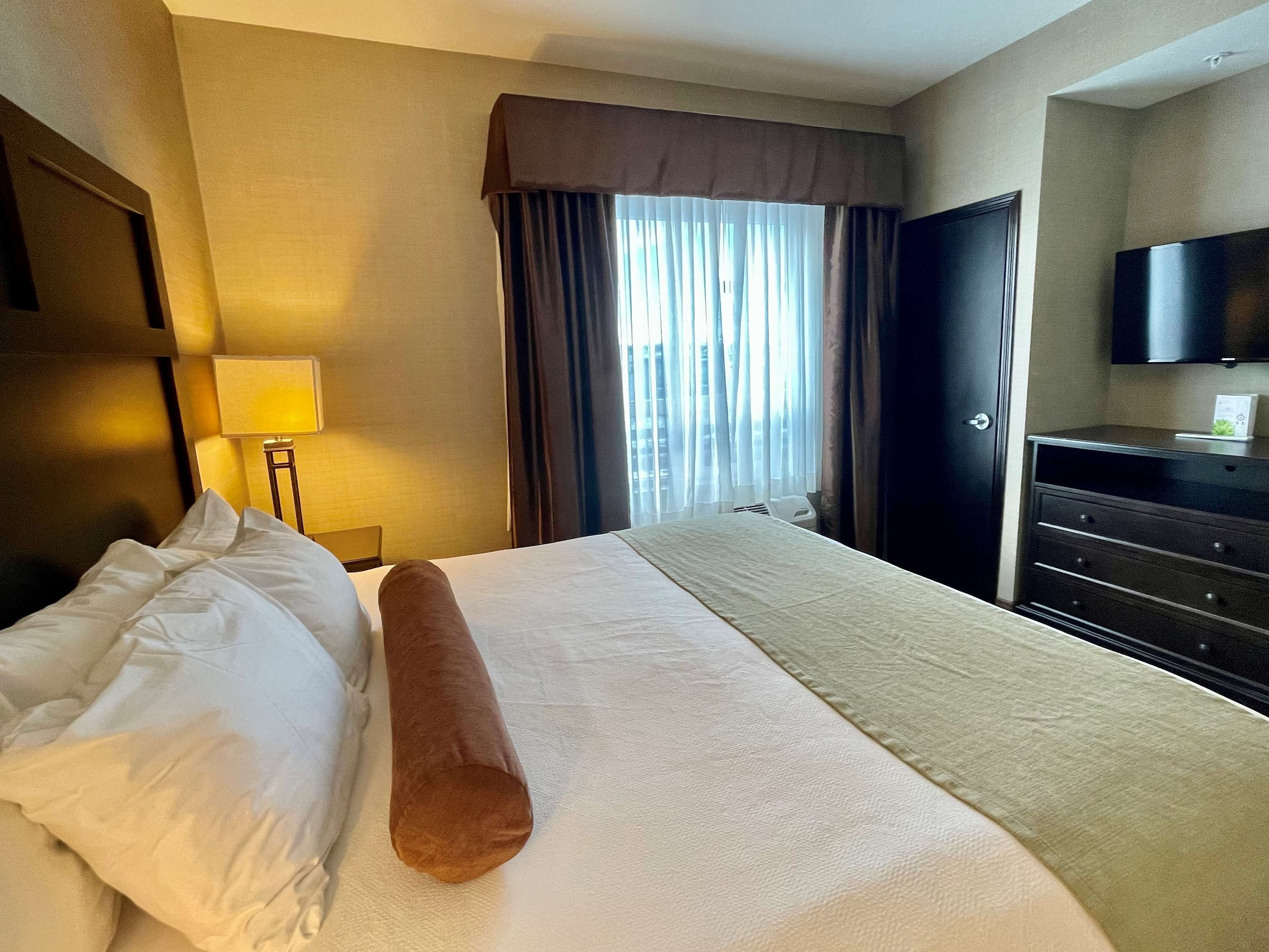 A hotel room with a bed, a nightstand, a lamp, a TV, and a window with curtains.