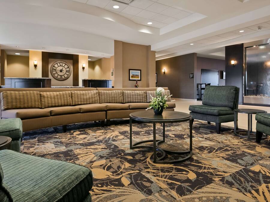A spacious lobby with a large sofa, a round coffee table, and two armchairs. A large wall clock and a framed picture are visible.