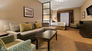 Habitación de hotel con sofá, sillón, cama y televisor.