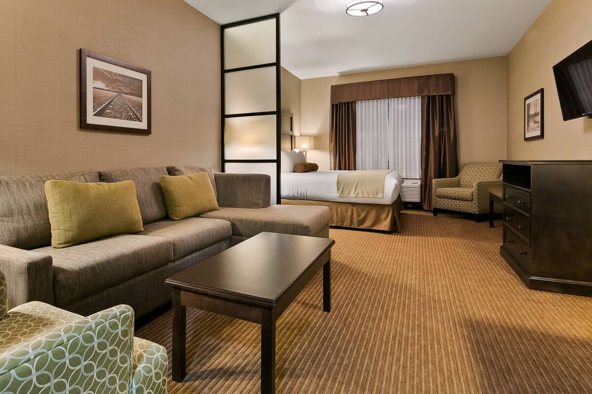 A hotel room with a sofa, armchair, bed, and a television.