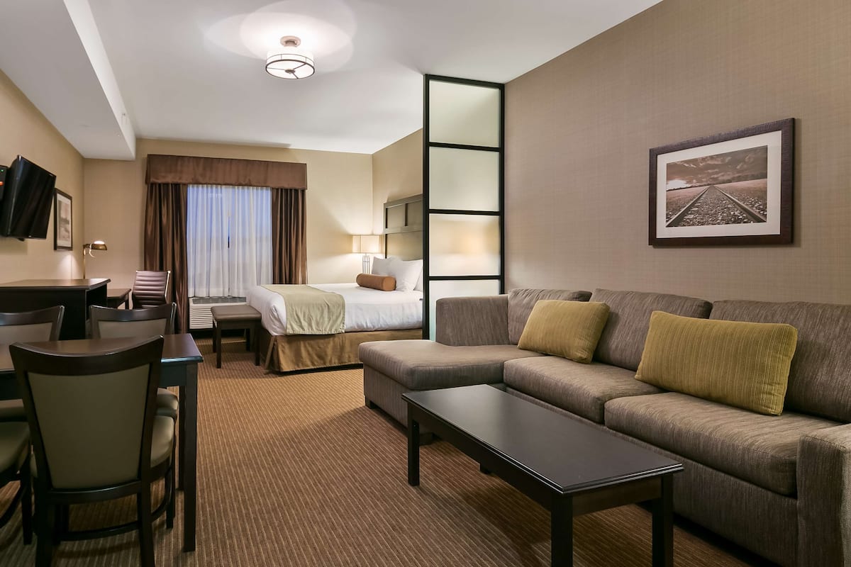A hotel room with a bed, a sofa, a desk with chairs, a coffee machine, and a TV.