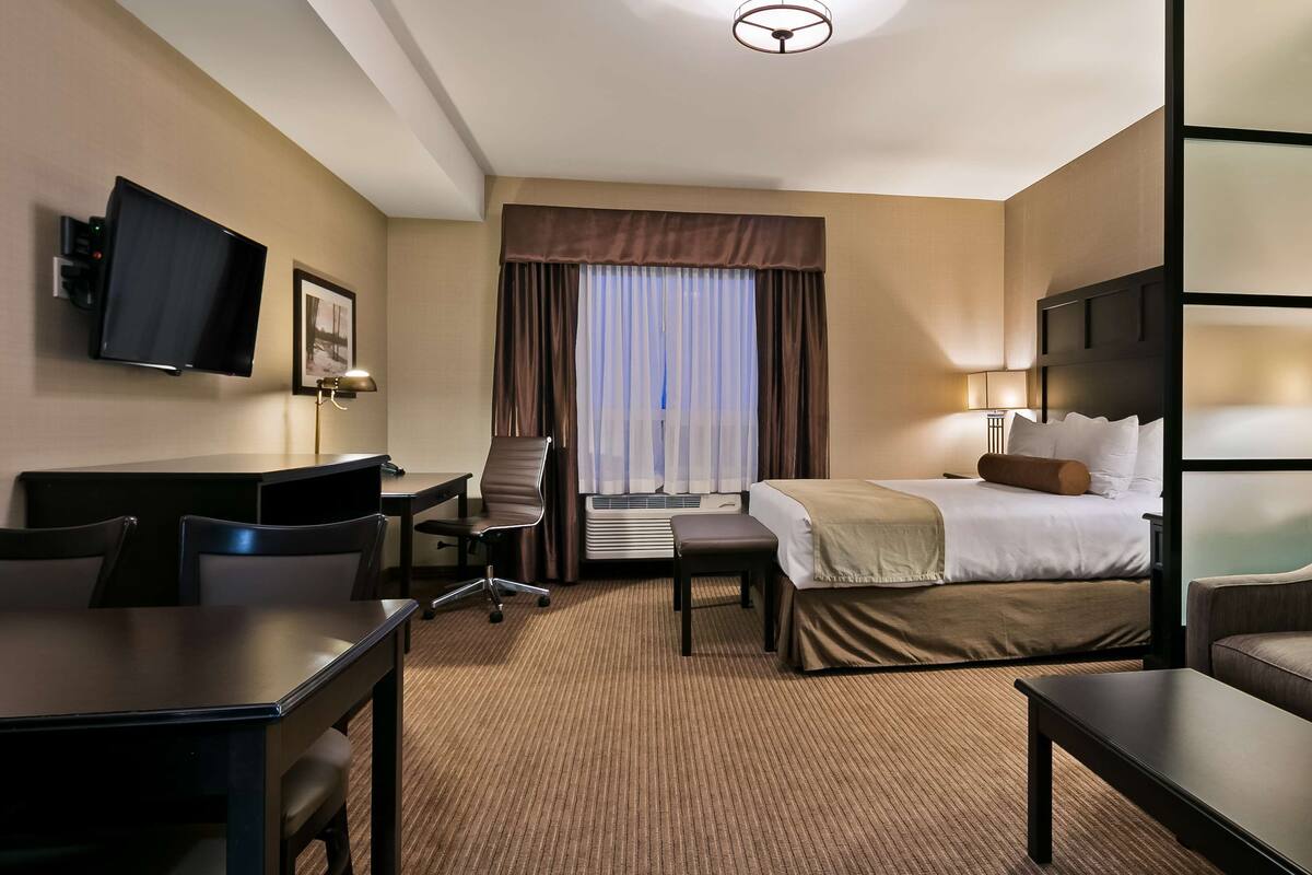 A hotel room with a bed, a desk, a chair, a sofa, a TV, and a window with curtains.