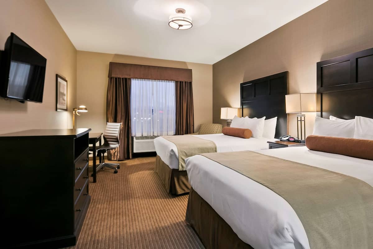 A hotel room with two beds, a desk, a chair, a television, and a window with curtains.
