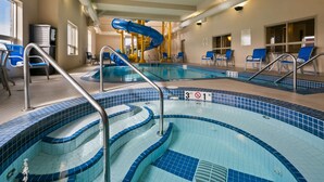 Una piscina interior con paredes de azulejos azules y blancos, un tobogán azul y un cartel de prohibido bucear.