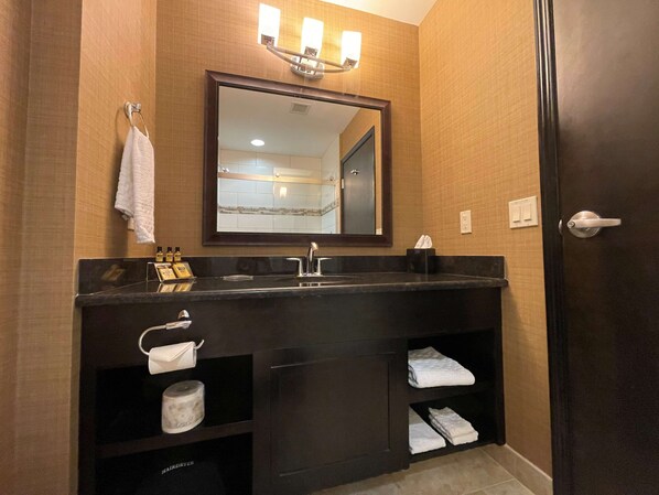 A bathroom with a dark vanity, a mirror, a towel rack, and a shelf with toiletries.