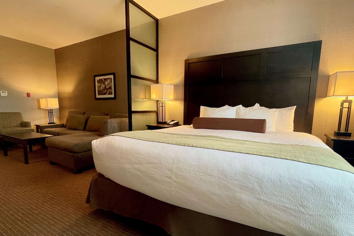 A hotel room with a large bed, two bedside tables, a chair, and a sofa.
