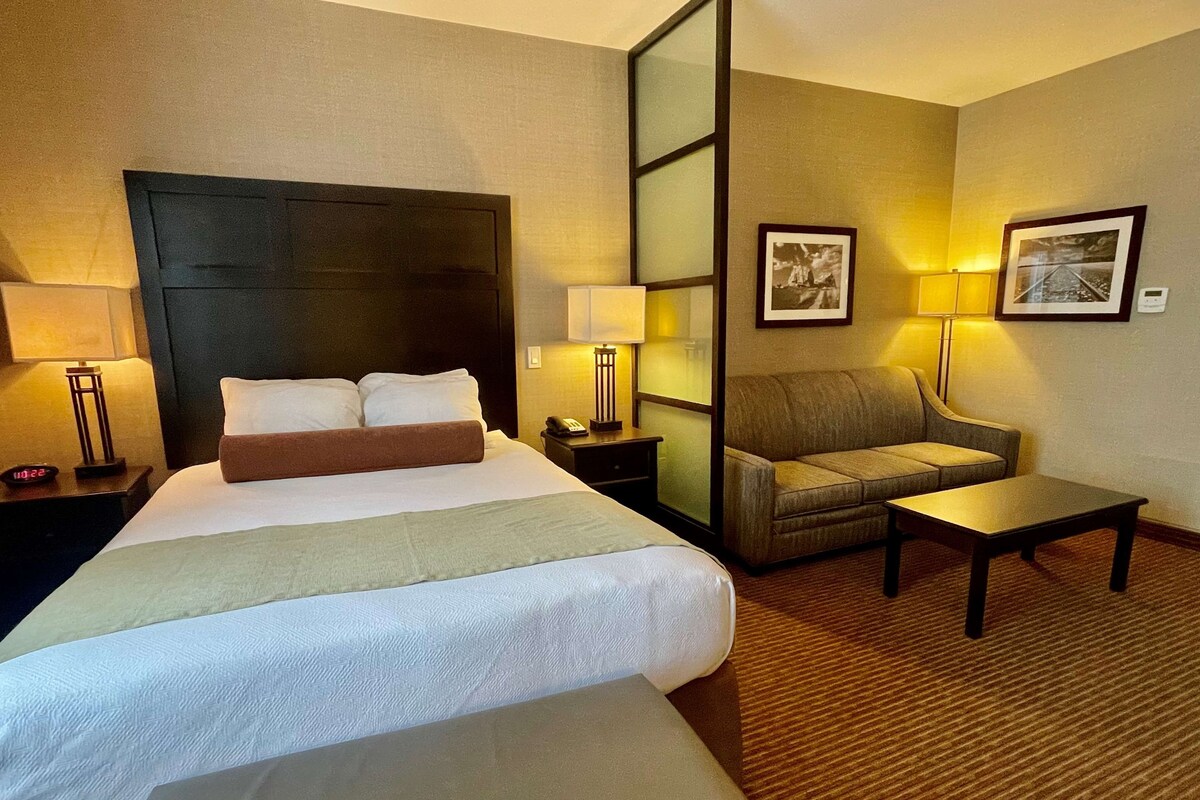 A hotel room with a large bed, a sofa, a small table, and two lamps.