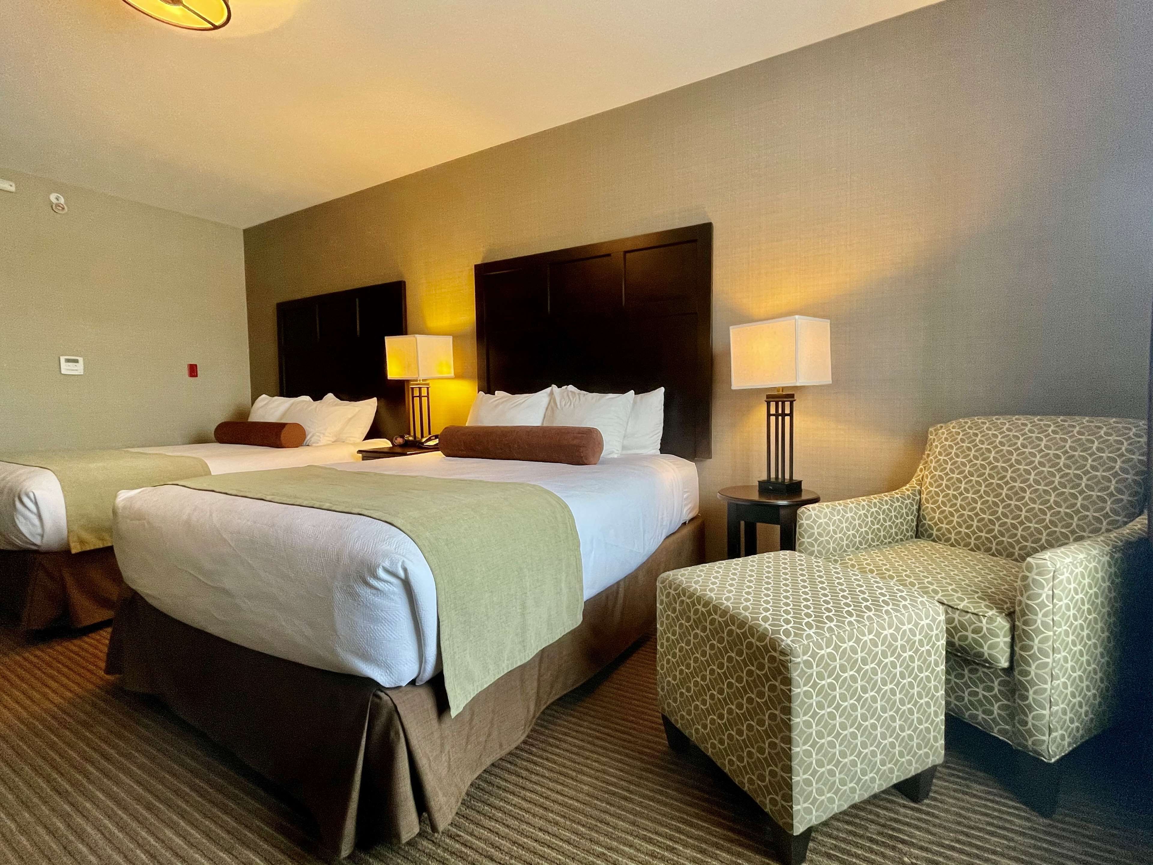 A hotel room with two beds, a sofa, a chair, and a lamp.