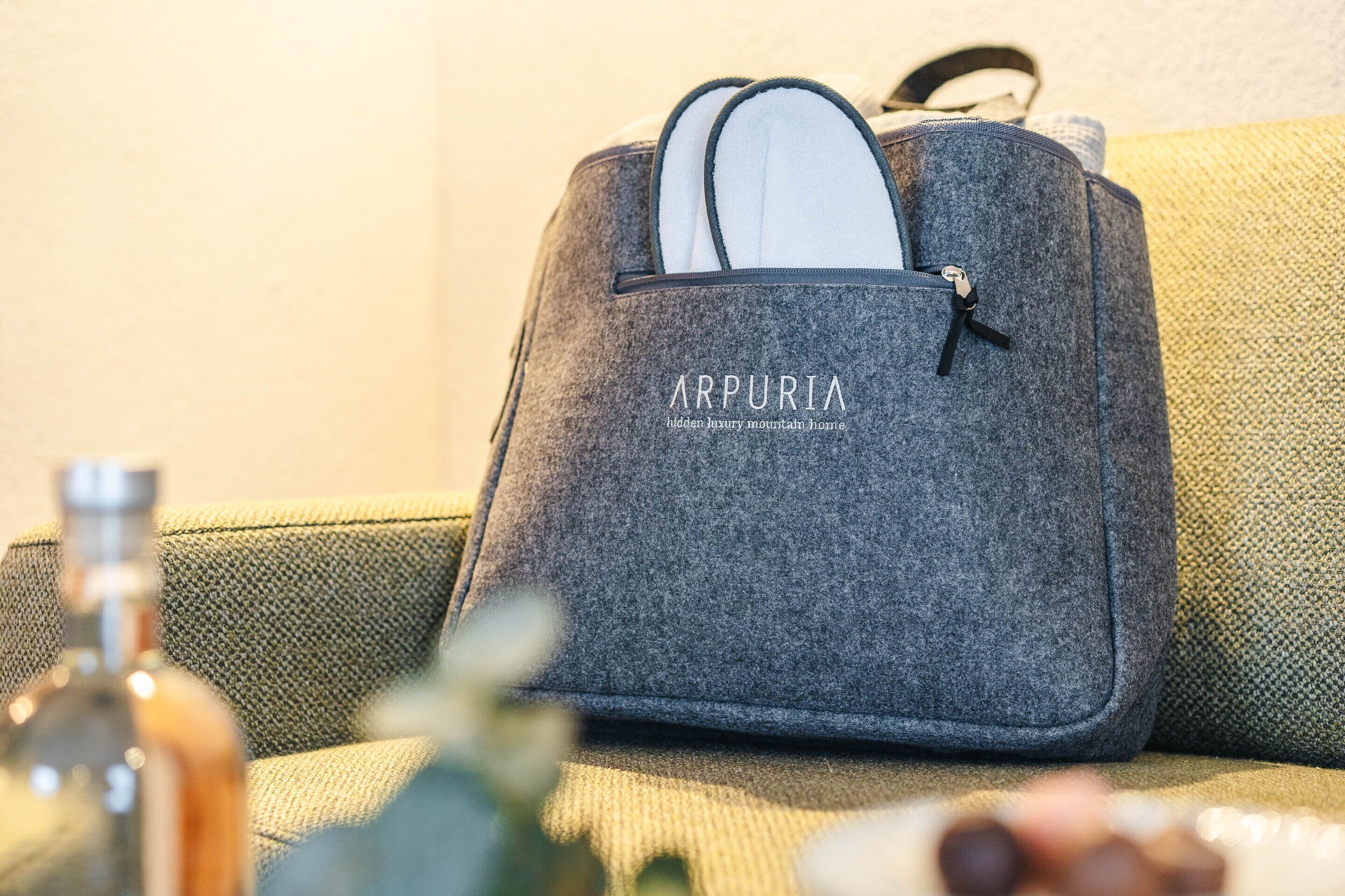A grey felt bag with the text "ARPUORIA" and "hidden luxury mountain home" on a green sofa.